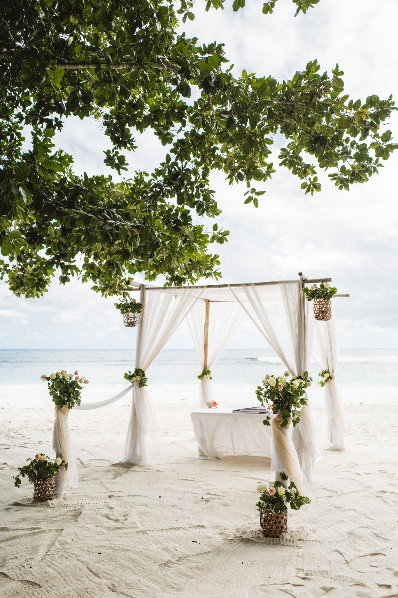 A wedding arch draped in white linen and tropical frangipani flowers on a pristine Seychelles beach — To Happy Endings ceremony design