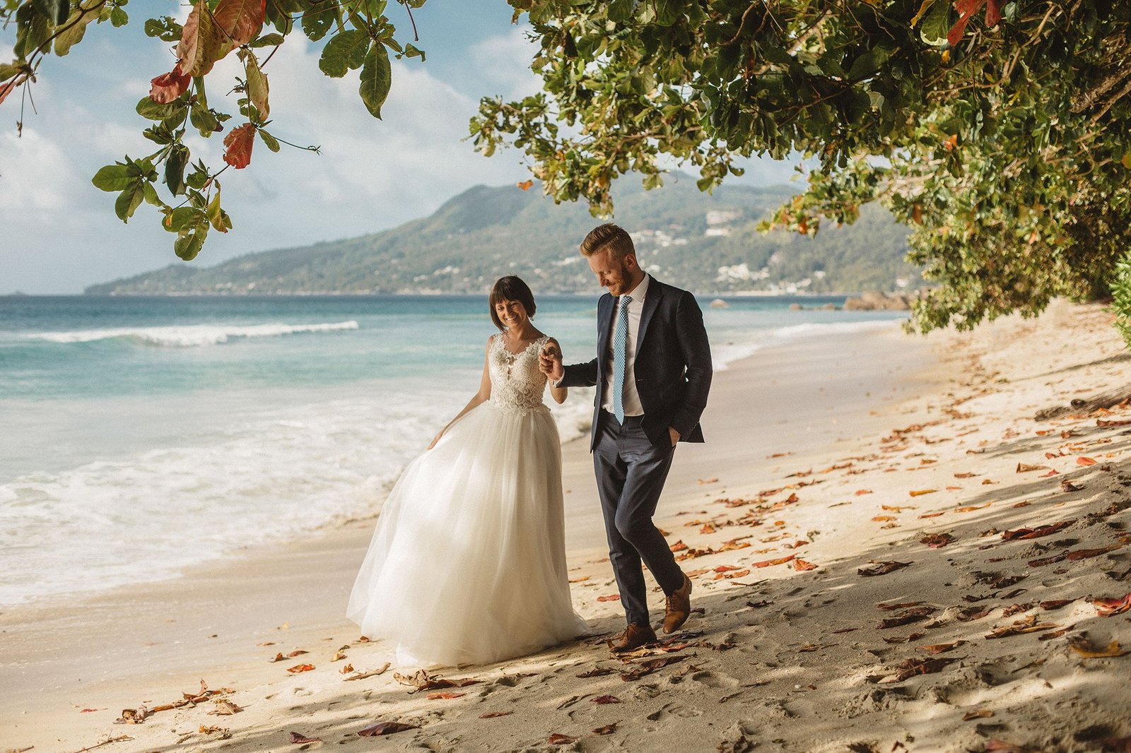 Couple embracing under tropical palm trees on a Seychelles beach — cinematic editorial wedding portrait